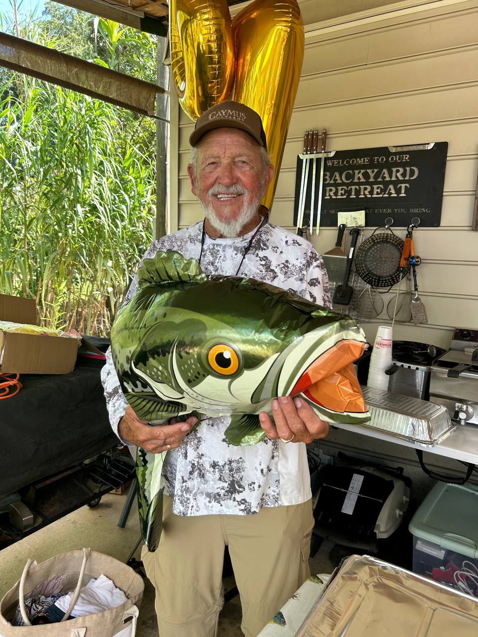 Captain Jim smiling on his birthday while holding a fish balloon at the backyard retreat
