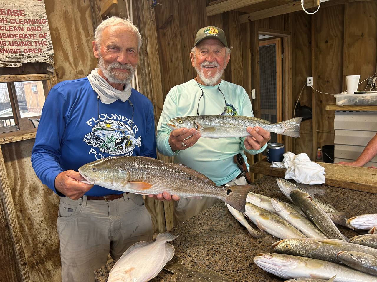 Two fishermen holding a redfish and speckled trout in a cleaning room