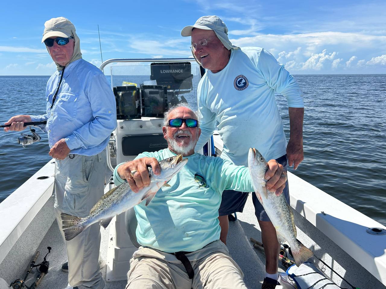 Three fishermen on a boat with Captain Jim holding two speckled trout