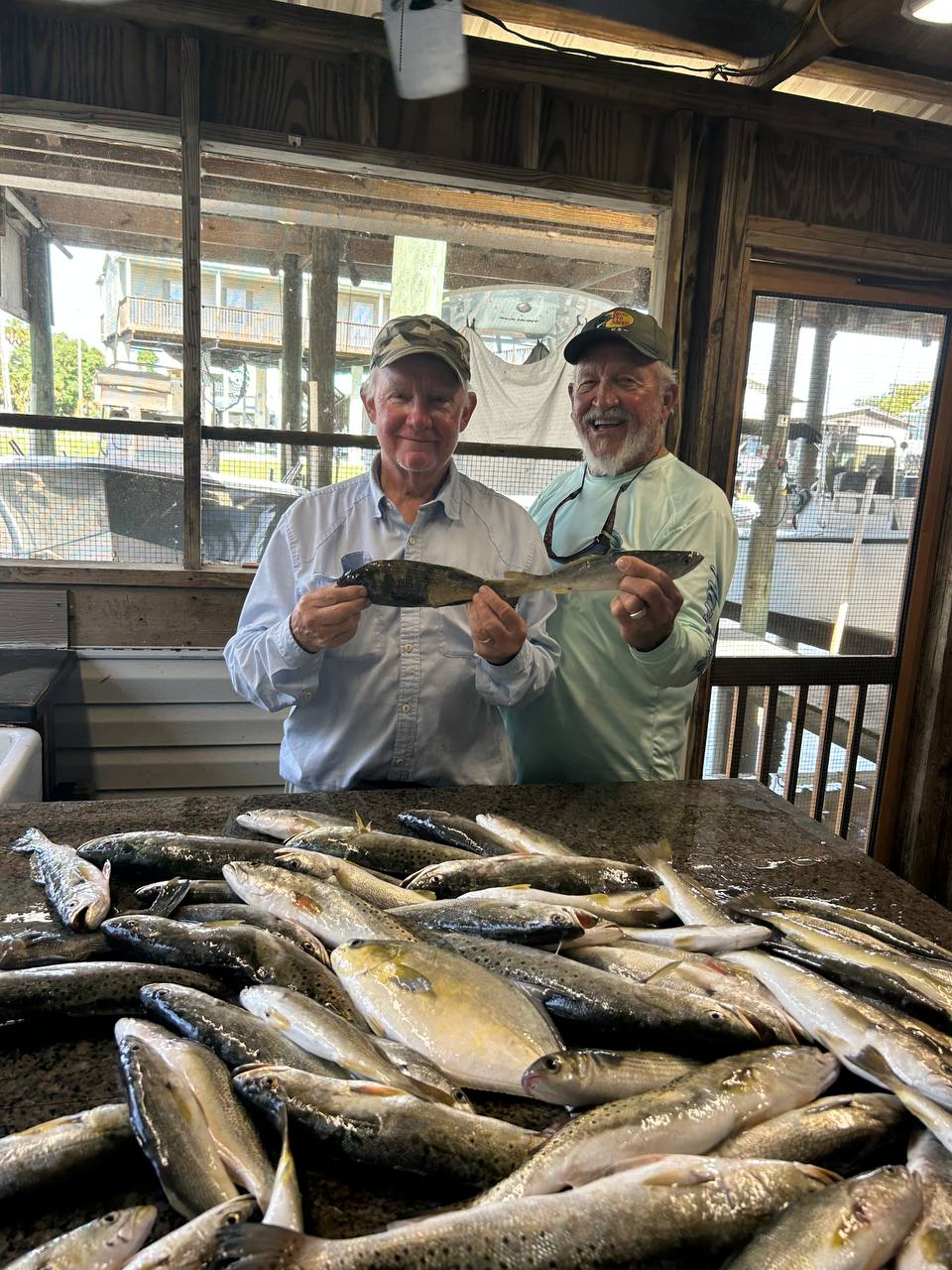 Captain Jim and a fishing partner smiling over a table full of trout and mixed coastal fish