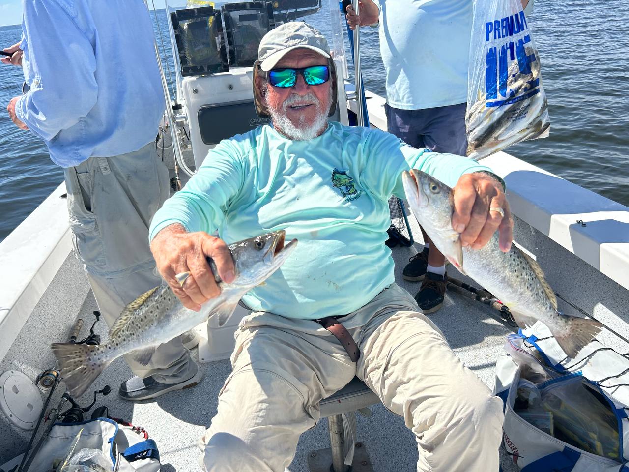 Captain Jim seated on the boat holding two speckled trout in bright sun